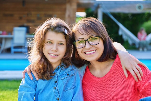 Retrato de una madre feliz y su hija adolescente mirando a la cámara Sonriendo abrazando a la madre y la niña juntos en el patio trasero cerca de la piscina al aire libre Concepto de estilo de vida de padre y hijo adolescente de la madre