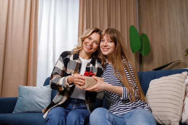 Retrato de madre feliz y su hija con caja de regalo en el sofá de la sala de estar