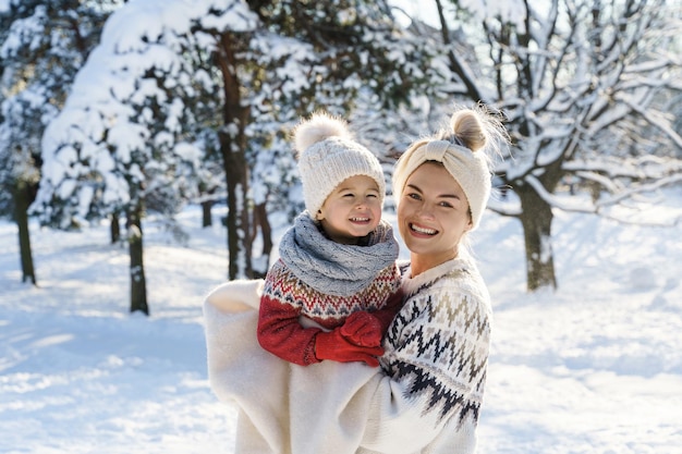 Retrato de madre feliz y su pequeño y lindo hijo usando suéteres cálidos durante el soleado día de invierno