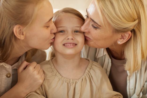 Retrato de madre y hermana besando a una niña linda en ambas mejillas, los lazos familiares y el concepto de generaciones