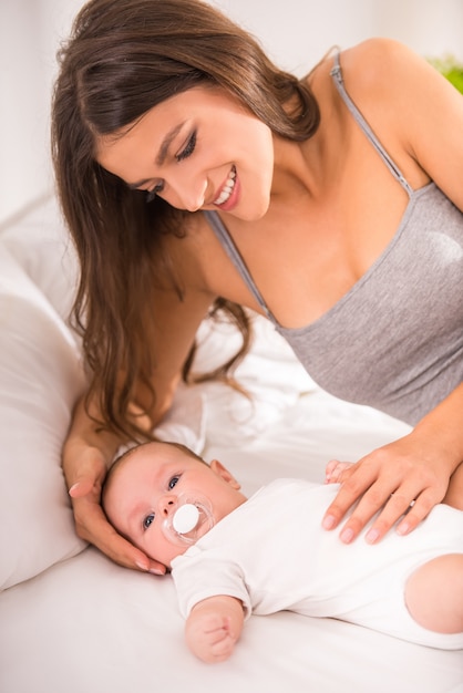 Retrato de la madre joven feliz con un bebé en la cama.