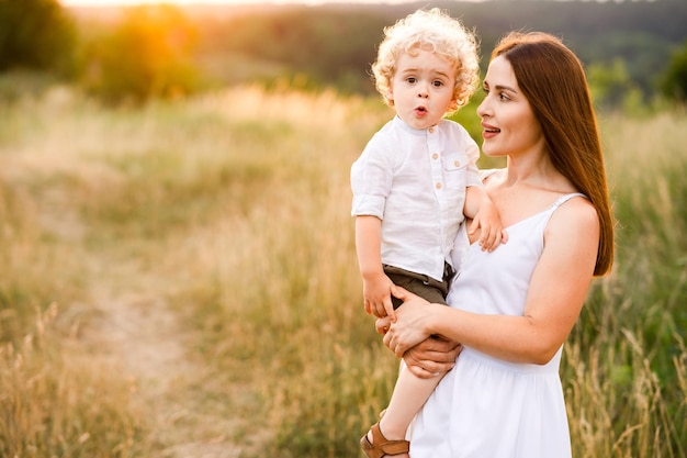 Retrato de madre con lindo hijo en sus brazos en la naturaleza