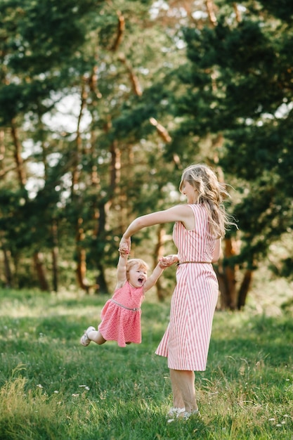 Retrato de una madre sostiene vomita y hace girar a la hija con las manos en la naturaleza en las vacaciones de verano Mamá y niña jugando en el parque al atardecer Concepto de familia amistosa Primer plano