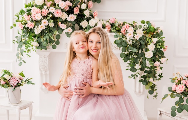 Retrato de una madre y su hija en elegantes vestidos en un hermoso interior con flores.
