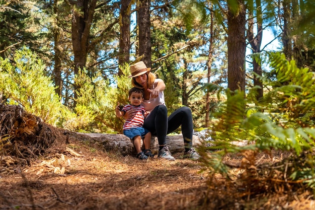 Retrato de una madre con su hijo sentado en un árbol en la naturaleza junto a pinos