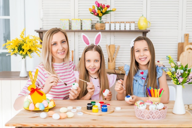 Retrato de una madre con sus hijas en la cocina. La familia pinta huevos. Preparando la Semana Santa en casa..