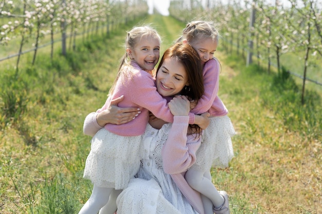 Retrato de una madre y sus hijas gemelas en un huerto de manzanos en flor Las niñas abrazan a su madre