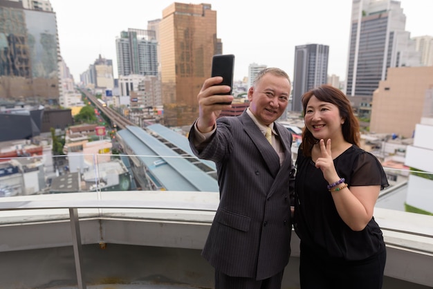 Retrato de maduro empresario japonés y madura mujer japonesa explorando la ciudad de Bangkok