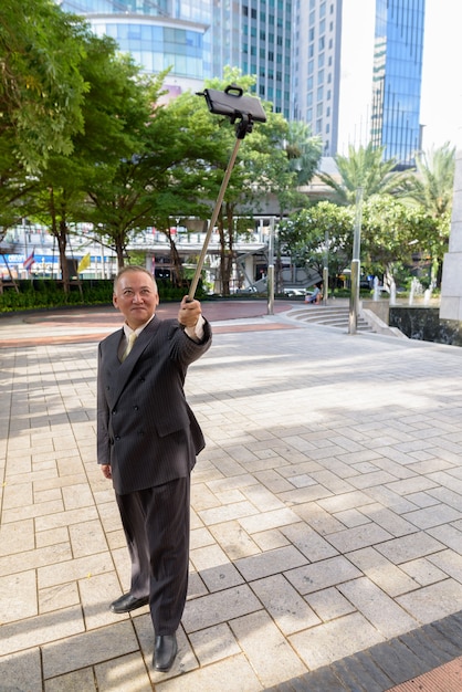 Retrato de maduro empresario japonés en traje explorando la ciudad de Bangkok