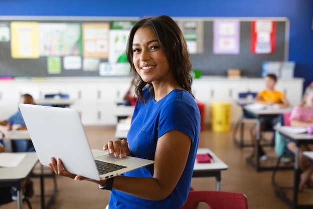 Retrato de una maestra afroamericana sosteniendo una laptop en la clase en la escuela