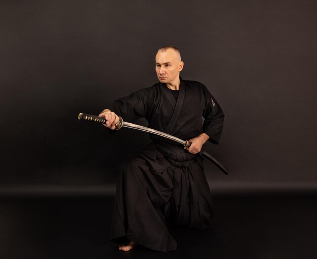 Foto retrato del maestro de aikido con cinturón de sensei negro en kimono de taekwondo con la espada katana en