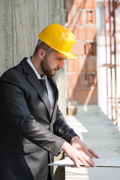 Foto retrato de maestro de la construcción con casco amarillo y blueprint en manos