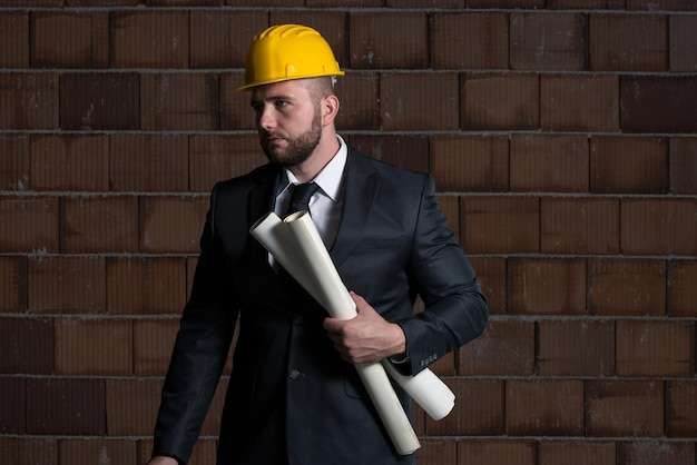 Retrato de maestro de la construcción con casco amarillo y Blueprint en manos