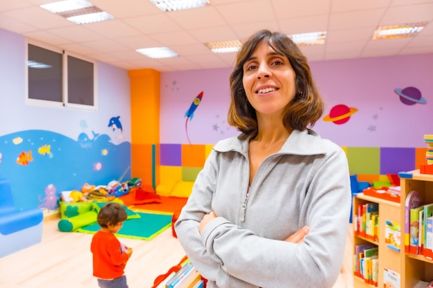 Foto retrato de un maestro de jardín de infantes o de educación infantil dentro de un jardín de infantes con un niño jugando en el fondo