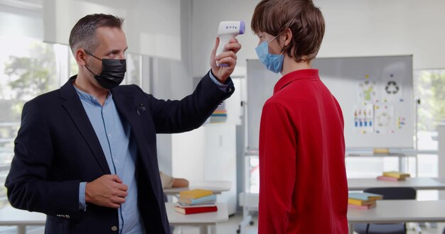 Foto retrato de un maestro que revisa la temperatura de los niños que ingresan al aula en la escuela