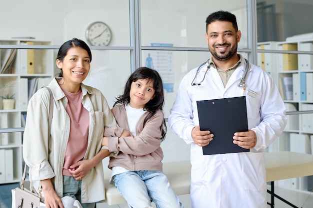 Retrato de mamá con niño sonriendo a la cámara junto con el pediatra en el consultorio