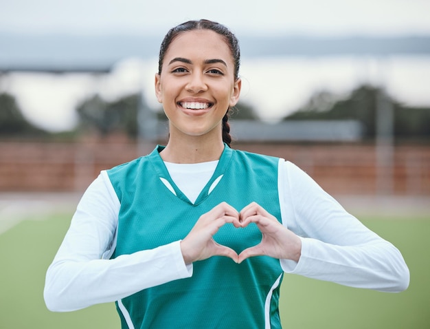 Retrato de manos de corazón o feliz con una mujer en el campo deportivo para ejercicio físico o entrenamiento para el bienestar Gesto de la mano con signo de amor o atleta saludable en un juego de entrenamiento para hockey o emoji con sonrisa