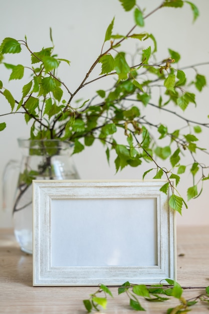 Retrato marco blanco sobre mesa de madera Jarrón de vidrio moderno con ramas verdes Estilo de vida ecológico