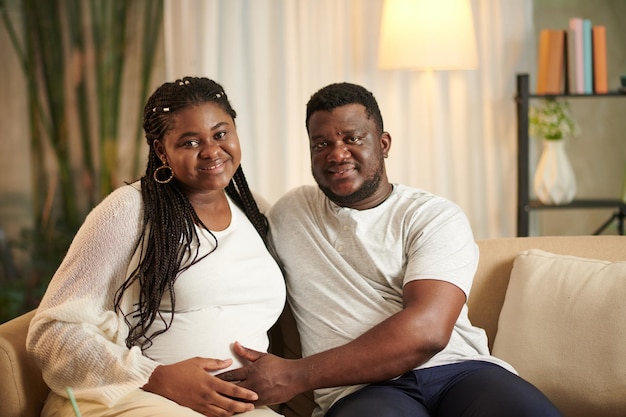 Retrato de un marido sonriente y su esposa embarazada sentados en el sofá en casa