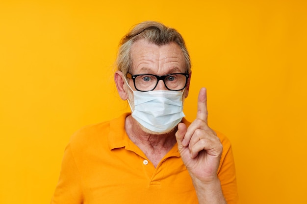 Retrato de una máscara médica feliz de un anciano en una camisa amarilla monocromática