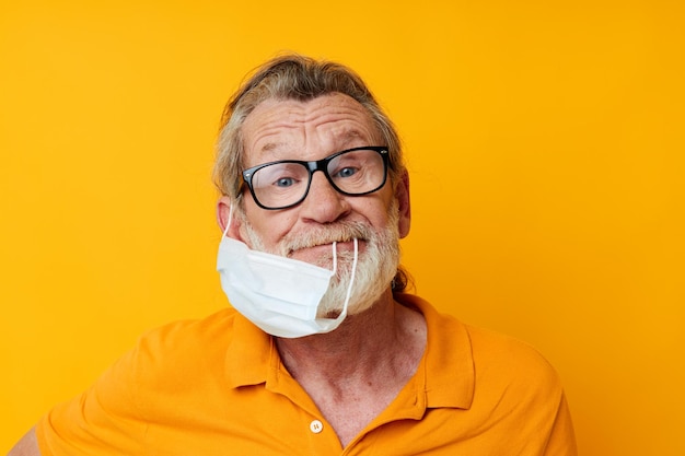 Retrato de la máscara médica del hombre mayor feliz en un fondo aislado de la camisa amarilla