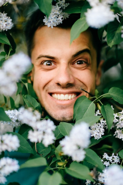 Retrato masculino em arbustos com flores com expressão engraçada.