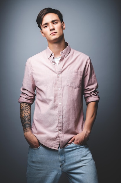 Retrato masculino sobre un fondo gris. Un joven con jeans azules y una camisa de fondo gris