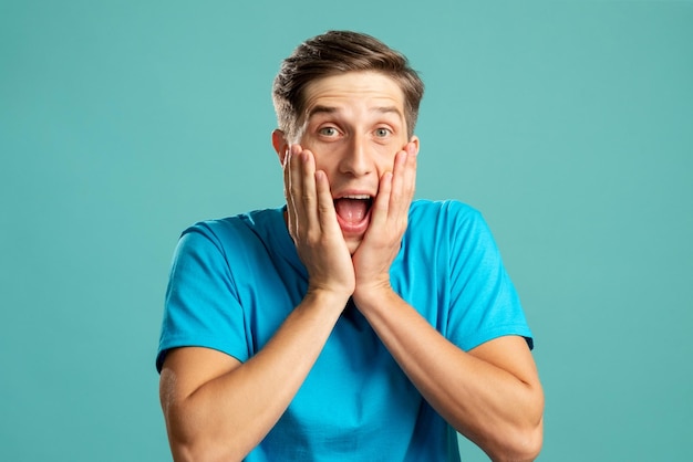 Retrato masculino surpreso Emoção expressiva Barbear cuidados com a pele Jovem animado positivo segurando o rosto olhando para a câmera isolada em azul