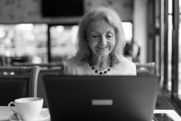 retrato, de, mayor, mujer anciana, sentado, y, utilizar la computadora portátil