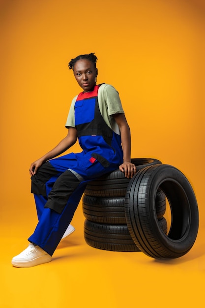 Retrato de una mecánica negra sonriente posando con neumáticos nuevos en el estudio