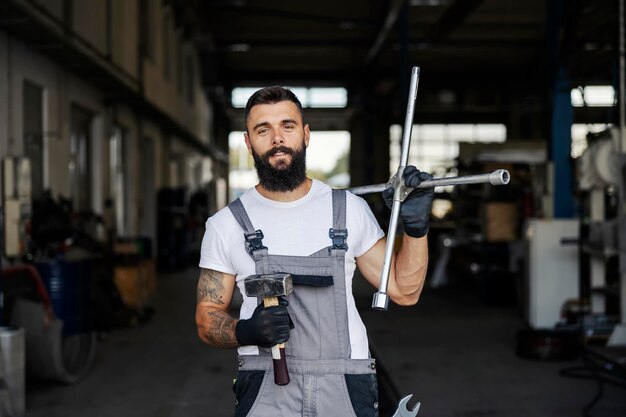 Retrato de un mecánico de automóviles sosteniendo herramientas y sonriendo a la cámara