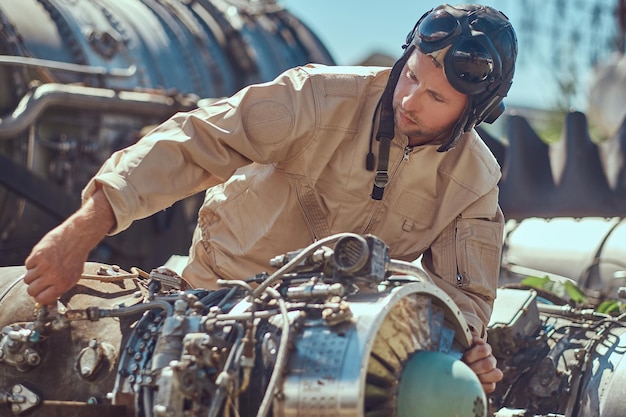 Retrato de un mecánico piloto con uniforme y casco volador, reparando la turbina del avión desmantelada en un museo al aire libre.