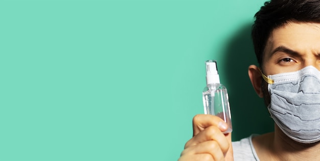 Retrato de media cara de chico joven con mascarilla médica, sosteniendo una botella dispensadora con gel antiséptico desinfectante contra las bacterias.