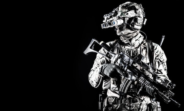Retrato a media longitud de las fuerzas especiales del ejército tirador comando soldado de élite equipado con auriculares tácticos de radio rifle de servicio armado usando gafas de visión nocturna en la oscuridad aislado en copyspace negro