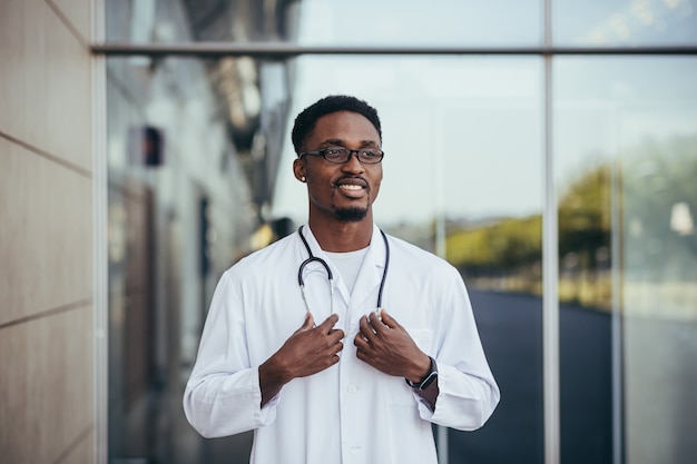 Retrato de un médico africano mirando a la cámara y sonriendo frente a la clínica