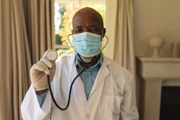 Foto retrato de un médico afroamericano de alto rango con una máscara facial que sostiene un estetoscopio