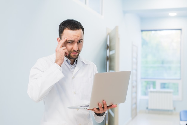 Retrato de médico alegre sentado en el escritorio trabajando en equipo portátil