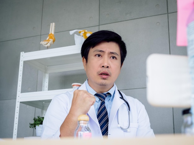Retrato de un médico asiático con uniforme blanco con un estetoscopio mirando la cámara en la pantalla de un teléfono móvil inteligente videollamada en línea y alentar al paciente Concepto médico y de telemedicina