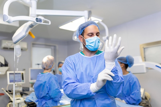 Retrato de médico cirujano masculino poniéndose guantes médicos de pie en la sala de operaciones Cirujano en la sala de operaciones moderna