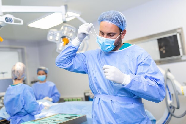 Retrato de médico cirujano masculino quitándose la máscara médica de pie en el quirófano Cirujano en el quirófano moderno