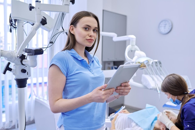 Retrato de médico dentista con tableta digital, mujer trabajando con computadora. Medicina de odontología sanitaria, clínica dental, visita del paciente y chequeo por antecedentes de dentista