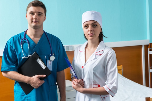 Retrato de médico con fonendoscopio en el cuello y enfermera en uniforme sosteniendo portapapeles mientras está de pie en la sala del hospital. Concepto de salud