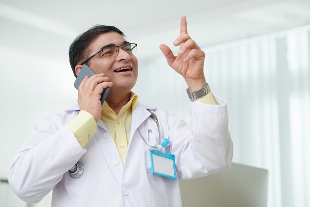 Retrato de un médico general maduro y emocionado que habla por teléfono con un paciente o un compañero de trabajo de otro hospital