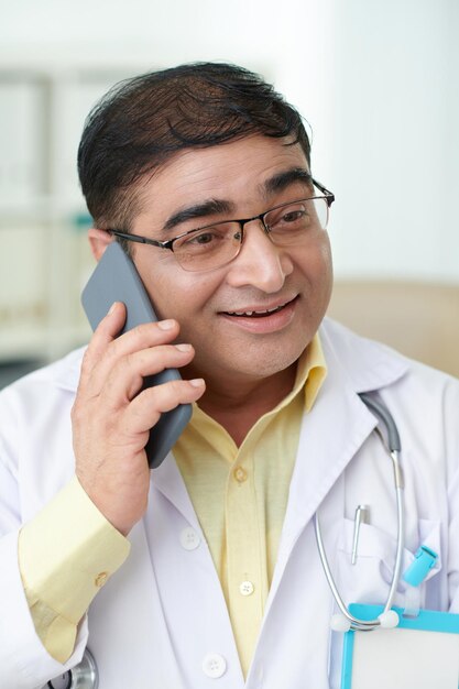 Retrato de un médico general positivo que responde una llamada telefónica del paciente