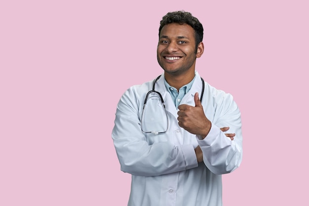 Retrato de un médico indio con estetoscopio mostrando el pulgar hacia arriba aislado en un fondo rosa