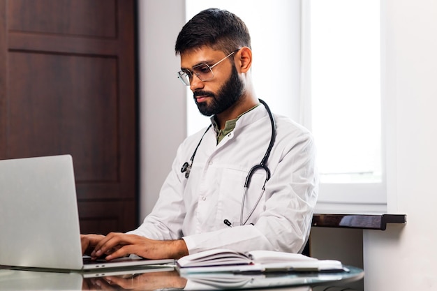 Retrato de un médico indio masculino con bata blanca en el consultorio de la clínica