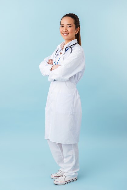 Retrato de un médico joven alegre feliz posando aislado sobre pared azul con estetoscopio.