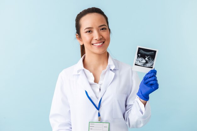 Retrato de un médico joven posando aislado sobre la pared azul con radiografía del bebé en las manos.