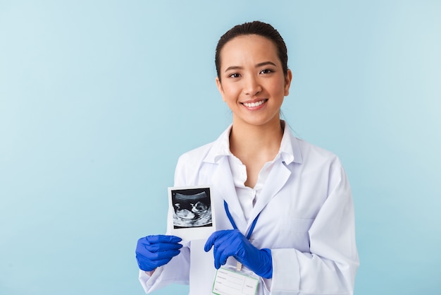 Retrato de un médico joven posando aislado sobre la pared azul con radiografía del bebé en las manos.