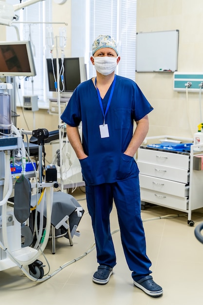 Retrato de un médico en máscara mirando a cámara sobre fondo de fondo de equipos médicos.